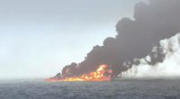 Burning oil tanker emitting black smoke at sea.