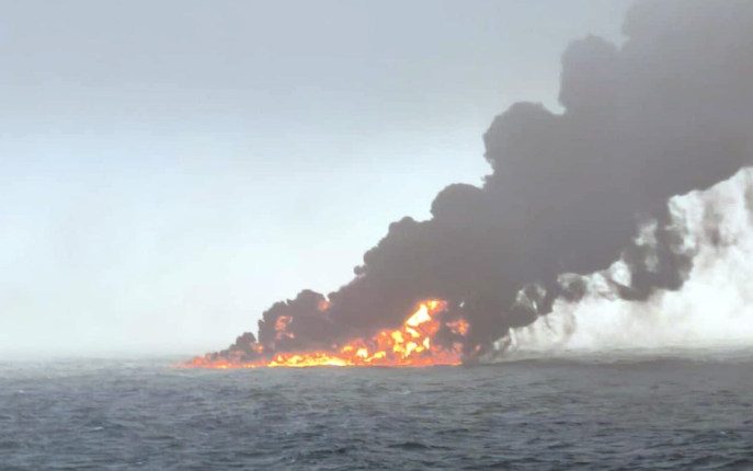 Burning oil tanker emitting black smoke at sea.