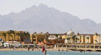 Windsurfer on a beach with a resort and mountains in the background.