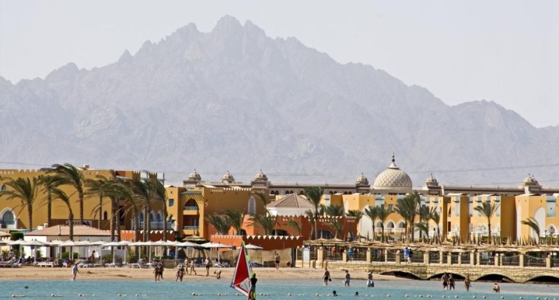 Windsurfer on a beach with a resort and mountains in the background.