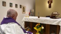 Priest in a wheelchair praying in a chapel.