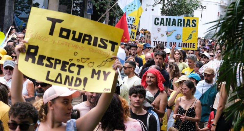 a crowd of people holding signs including one that says tourist respect my land