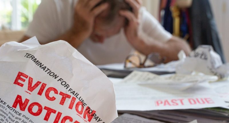Eviction notice in foreground, stressed man in background.