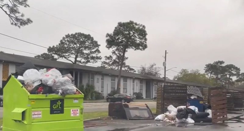 Overfilled dumpsters and trash overflowing in a Jacksonville apartment complex parking lot.