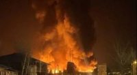 Large fire engulfing a building at night, with people walking away.