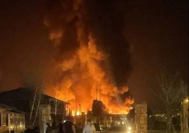 Large fire engulfing a building at night, with people walking away.