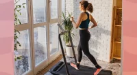 woman walking on treadmill in apartment in front of floor-to-ceiling windows