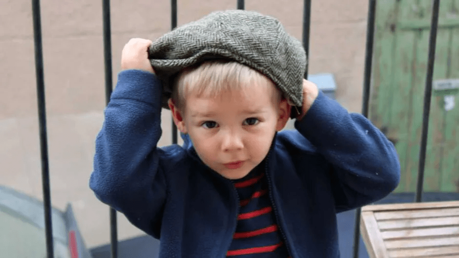 Toddler putting on a newsboy cap.