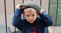 Toddler putting on a newsboy cap.