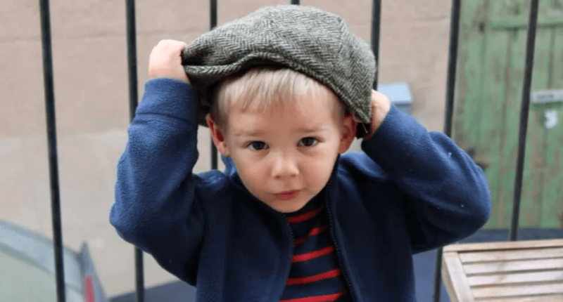 Toddler putting on a newsboy cap.