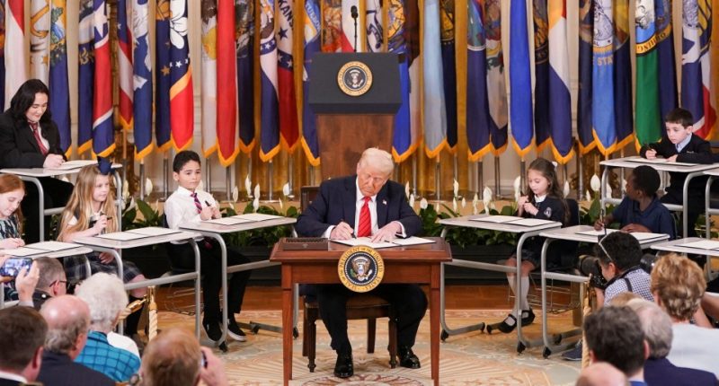 President Trump signing an executive order to shut down the Department of Education, surrounded by children.
