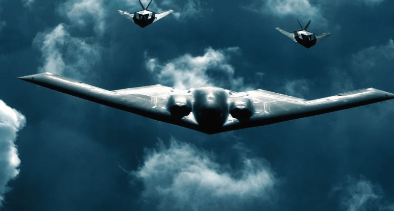 B-2 Spirit bomber with two fighter jets flying in formation.