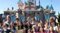 A large family posing for a photo in front of Sleeping Beauty's Castle at Disneyland.  The faces of most family members have been blurred.
