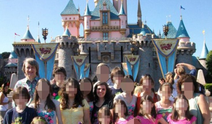 A large family posing for a photo in front of Sleeping Beauty's Castle at Disneyland.  The faces of most family members have been blurred.