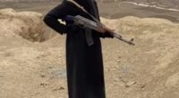 Woman in black coat holding an AK-47 rifle in Afghanistan.