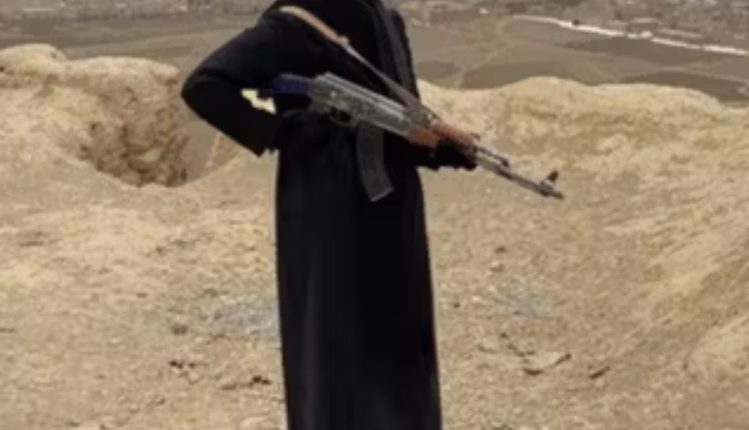Woman in black coat holding an AK-47 rifle in Afghanistan.