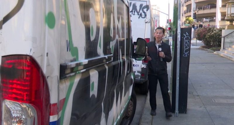 A reporter stands by a USPS van covered in graffiti.