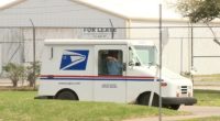 A USPS mail truck parked on a grassy area.