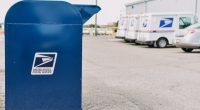 USPS postal box with USPS trucks in the background.
