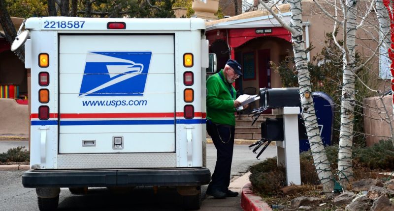 A postal worker delivers mail from a USPS truck.