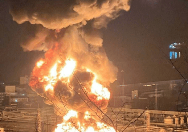 Large fire engulfing industrial storage tanks at night.