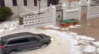 A car driving through a street flooded with hail and water.
