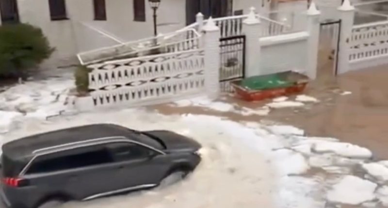 A car driving through a street flooded with hail and water.