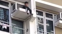 Two boys sitting on a high-rise window ledge.