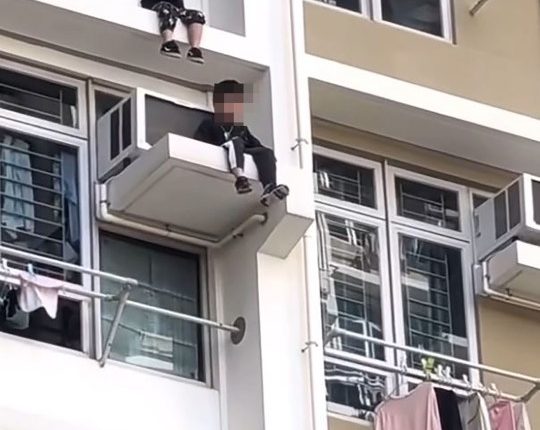 Two boys sitting on a high-rise window ledge.