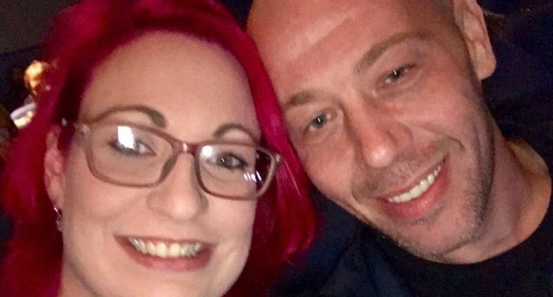 Close-up selfie of a woman with pink hair and glasses and a man.