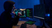 Person on phone, pointing at computer screens displaying code.