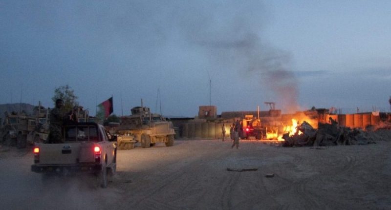 An Afghan National Army pickup truck passes parked U.S. armored military vehicles, as smoke rises from a fire in a trash burn pit at Forward Operating Base Caferetta Nawzad, Helmand province south of Kabul, Afghanistan, April 28, 2011. (AP Photo/Simon Klingert, File)