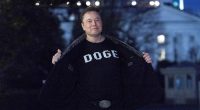Elon Musk flashes his t-shirt that reads "DOGE" to the media as he walks on South Lawn of the White House, in Washington, Sunday, March 9, 2025.