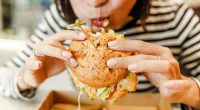 Woman eating a hamburger in modern fastfood cafe, lunch concept