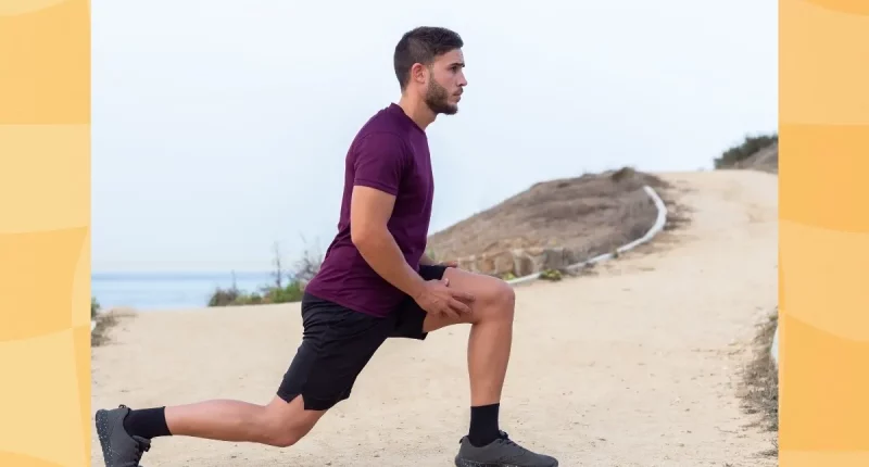 man in maroon t-shirt and black shorts doing walking lunges outdoors by the beach
