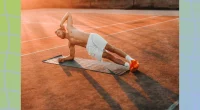 fit man doing a side plank on mat on court while sun sets
