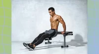 muscular man doing tricep dips from workout bench in front of gray backdrop