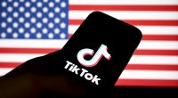 TikTok logo on a phone screen in front of a blurred US flag.