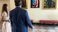 Two people view portraits of Kelly Loeffler, Donald Trump, and another woman in the White House.