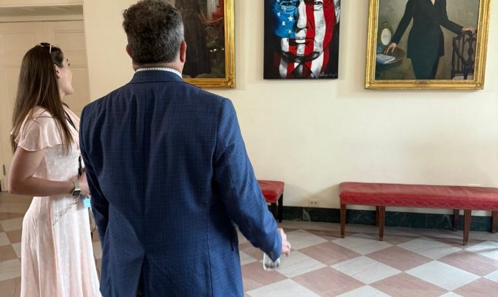 Two people view portraits of Kelly Loeffler, Donald Trump, and another woman in the White House.