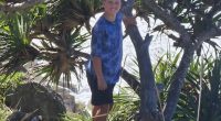Boy standing by a pandanus tree near the ocean.