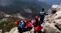 Rescue workers attending to a paragliding accident victim on a rocky mountainside.