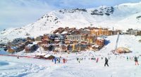Skiers and snowboarders on a snowy slope near a village in the Alps.