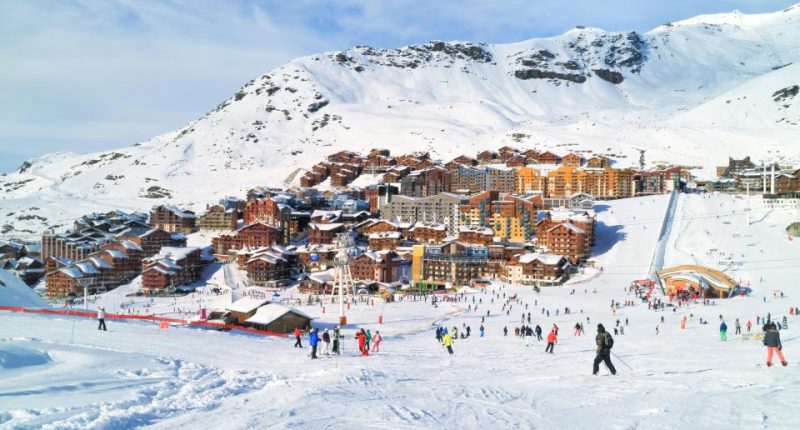 Skiers and snowboarders on a snowy slope near a village in the Alps.