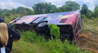 An overturned bus on its side, with people standing nearby.