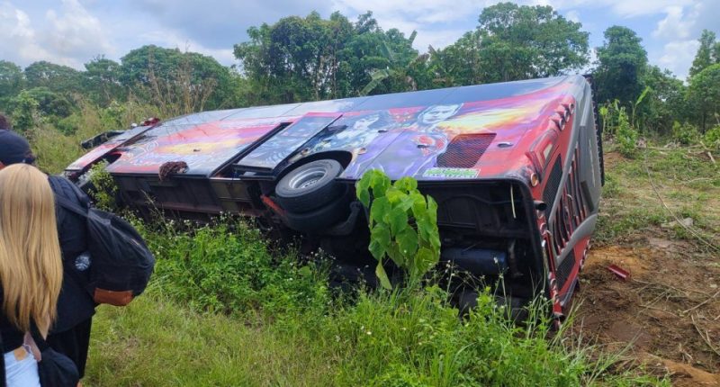 An overturned bus on its side, with people standing nearby.