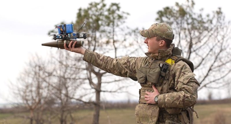A soldier holding a drone modified for carrying a projectile.