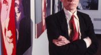 Andy Warhol standing in front of his artwork.