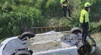 Upside-down supercar in a ditch with emergency personnel nearby.