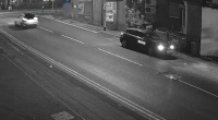Nighttime security camera footage of a street with two cars.